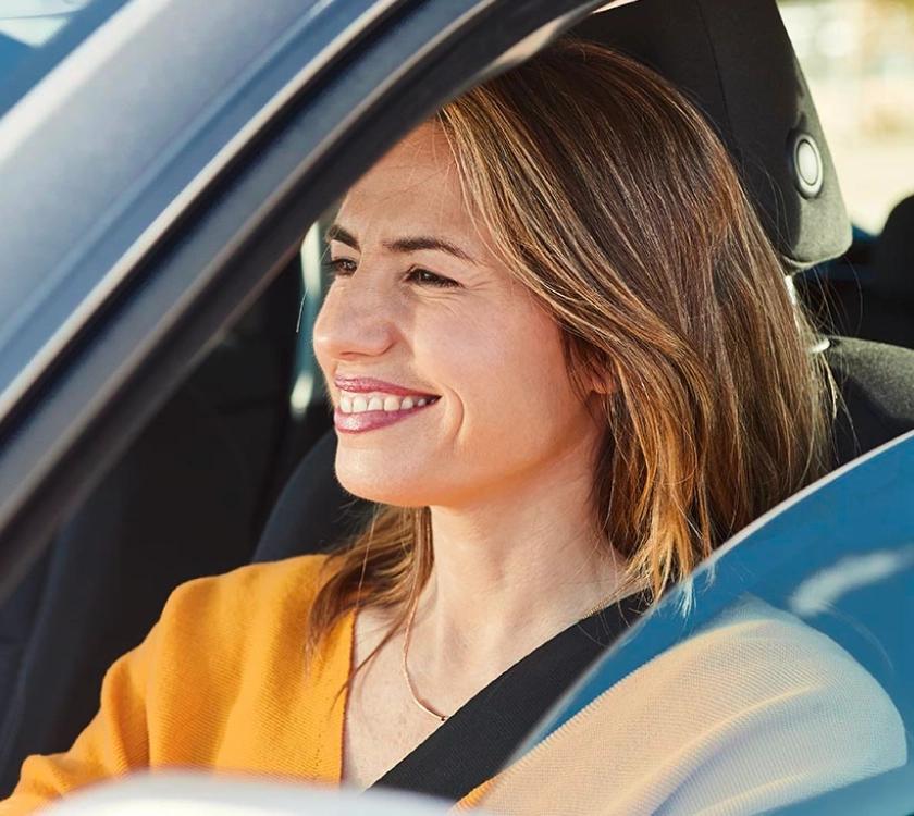Μια γυναίκα χαμογελάει ενώ κάθεται στη θέση του οδηγού ενός αυτοκινήτου.