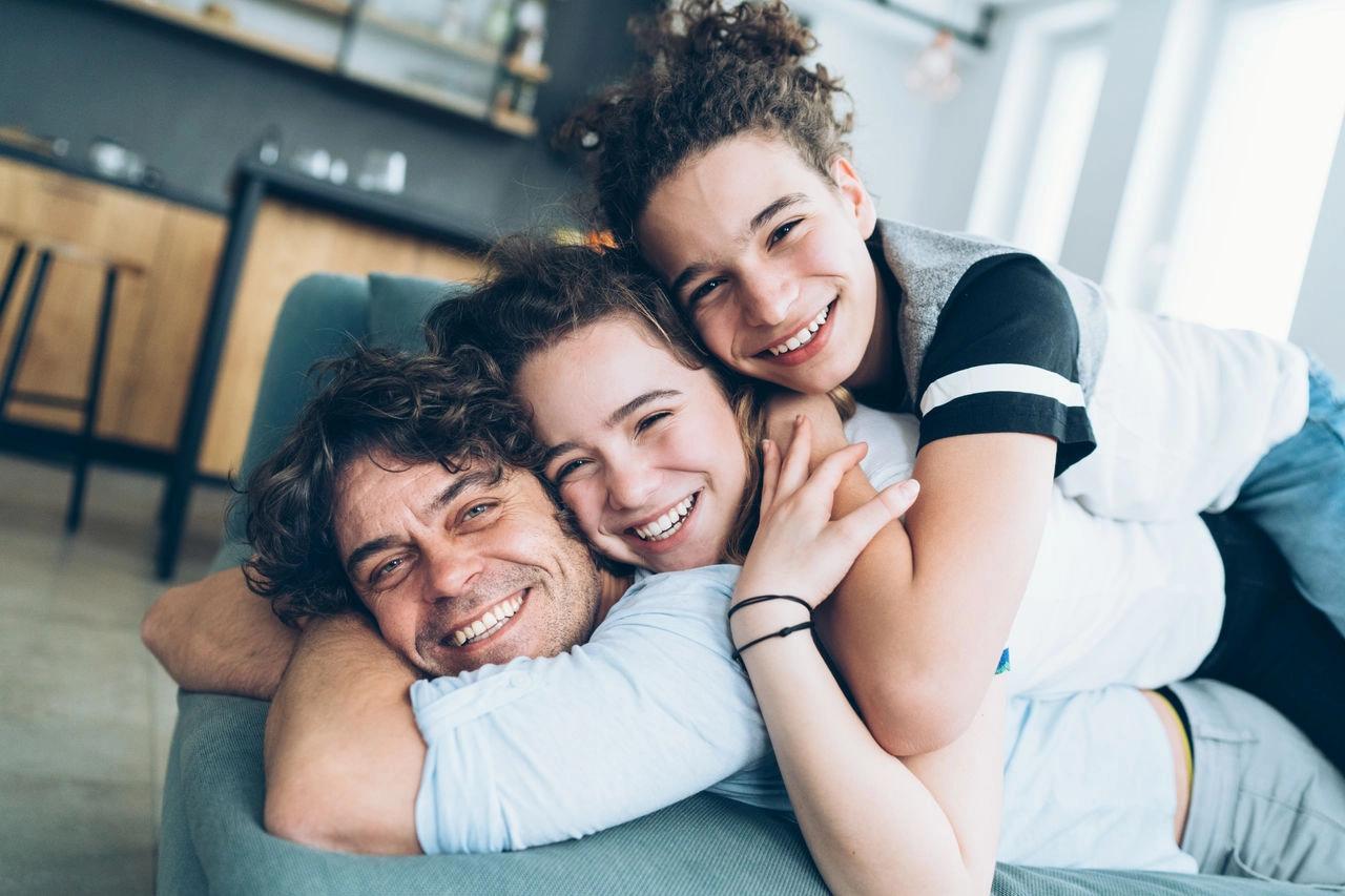 ένας άντρας και δύο παιδιά αγκαλιάζονται πάνω σε έναν καναπέ.